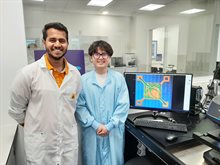 Student and his supervisor, both in lab coats, standing next to a computer screen showing a chip package design