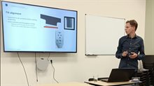 Young man presenting his thesis project stands in front of a slide titled Tilt alignment