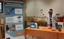 Young man in lab coat standing in a booth with chip packaging examples and a tiny microscope