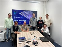 Seven men in a meeting room standing in front of a screen showing the meeting's title: Sinter workshop