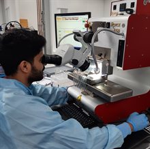 Young man in lab coat looking intently through a microscope of a wirebond tester