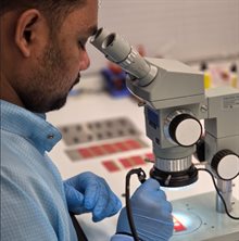 Young man in lab coat working on a chip package underneath a microscope