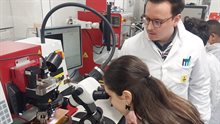 Young girl peering through microscope under supervision of scientist